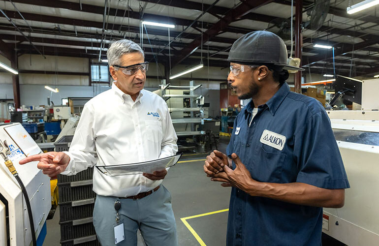 Alkon CEO Rahul Deshmukh speaks with Bryan Harvey, a member of the machining team, on the production floor.